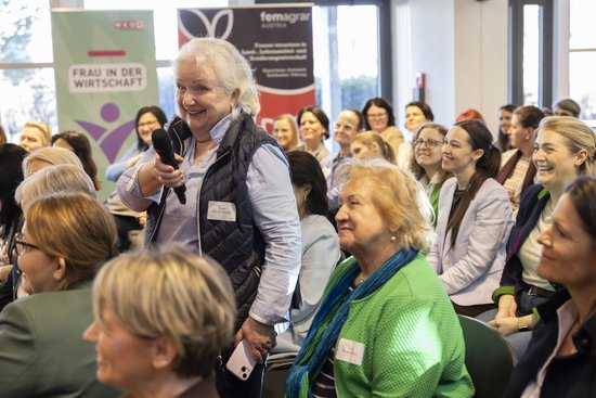 Adult,  Chair,  Crowd,  Female,  Glasses,  Microphone,  Necklace,  People,  Person,  Woman